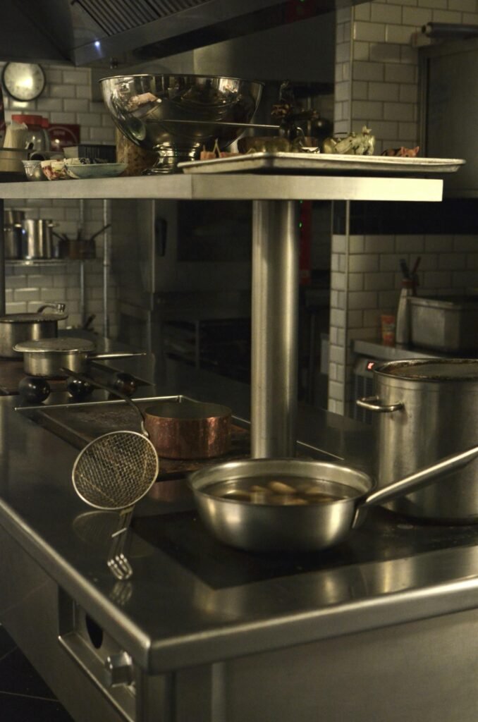 Industrial kitchen scene with pots and a fryer on a stainless steel stove.